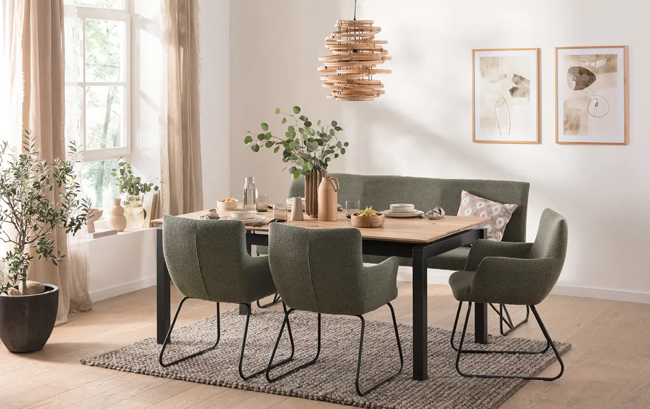 Holztisch mit sechs grünen Polsterstühlen, Teppich, Pflanzen und Bildern an der Wand
